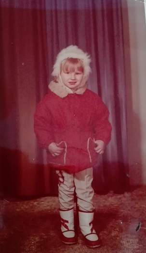 Dziewczynka w futrzanej czapce, zimowej kurtce i kozaczkach pozuje na tle czerwonej zasłony. Zdjęcie z połowy lat osiemdziesiątych XX wieku.
